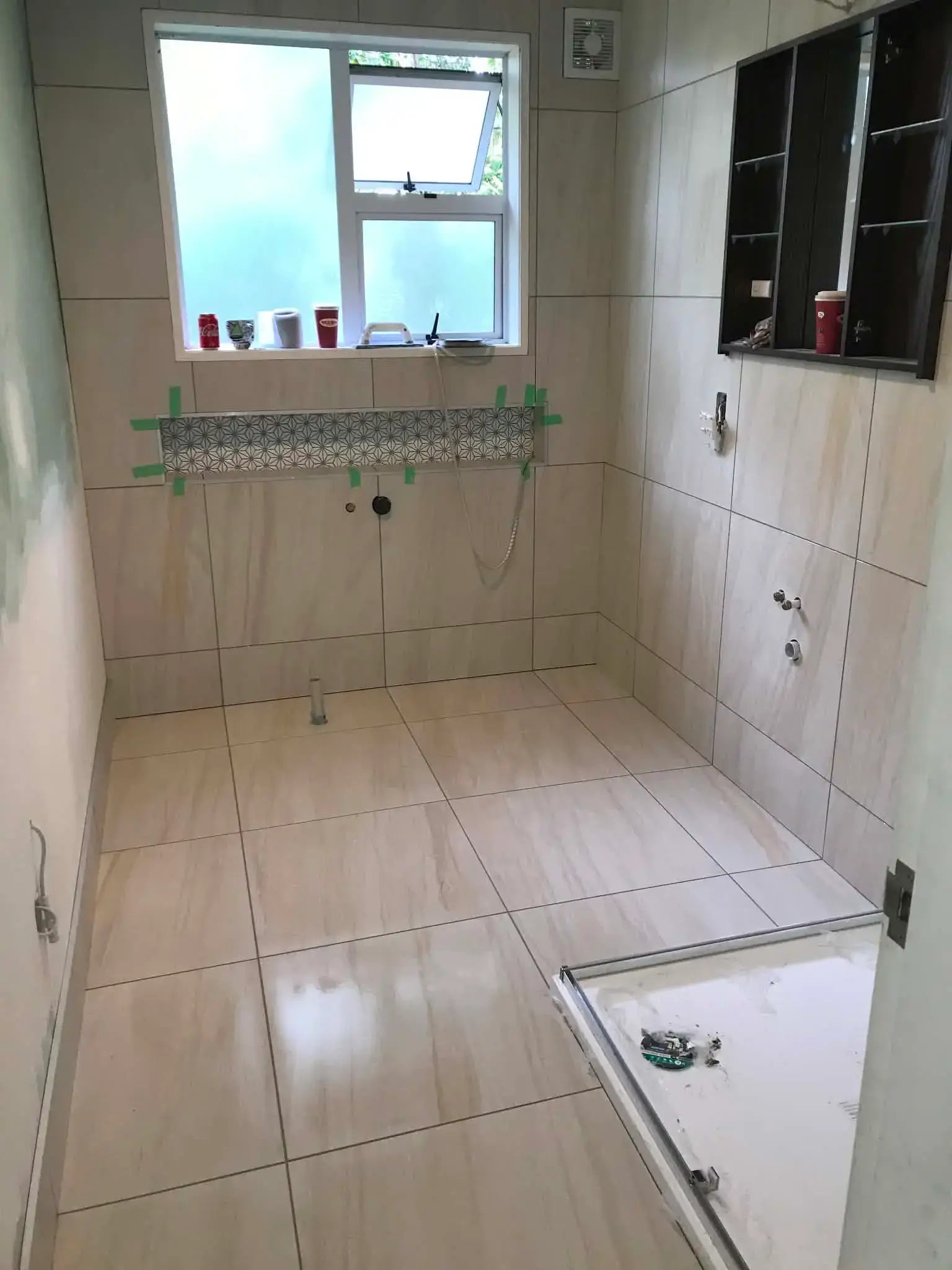 Bathroom floor tiling in beige stone-look porcelain with a patterned feature strip inset at wall height