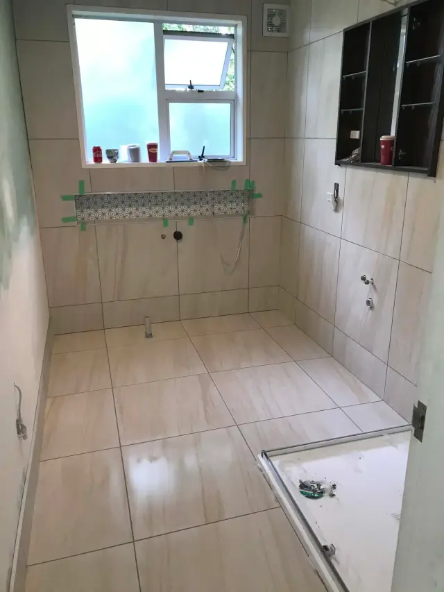 Bathroom floor tiling in beige stone-look porcelain with a patterned feature strip inset at wall height