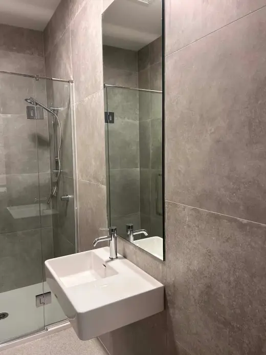 Finished ensuite with large-format grey porcelain wall tiles, frameless glass shower and wall-hung basin, tiled by ROH Tiling in Wellington