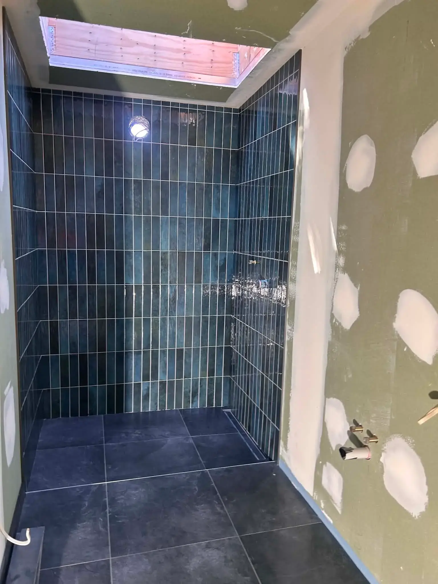 Walk-in shower with teal vertical stack-bond wall tiles, dark large-format floor tiles and a linear drain, under a skylight
