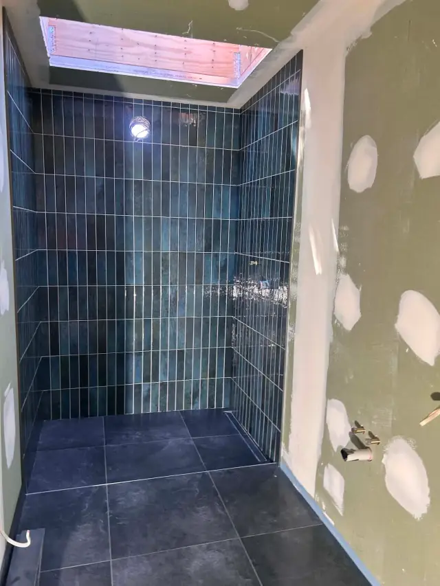 Walk-in shower with teal vertical stack-bond wall tiles, dark large-format floor tiles and a linear drain, under a skylight