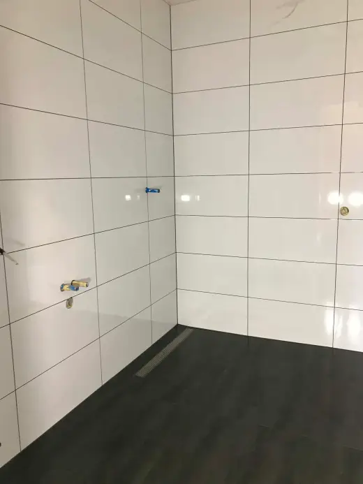 Shower with white gloss wall tiles, dark floor tiles and a stainless linear drain