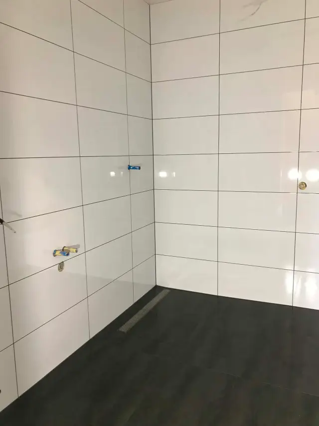 Shower with white gloss wall tiles, dark floor tiles and a stainless linear drain