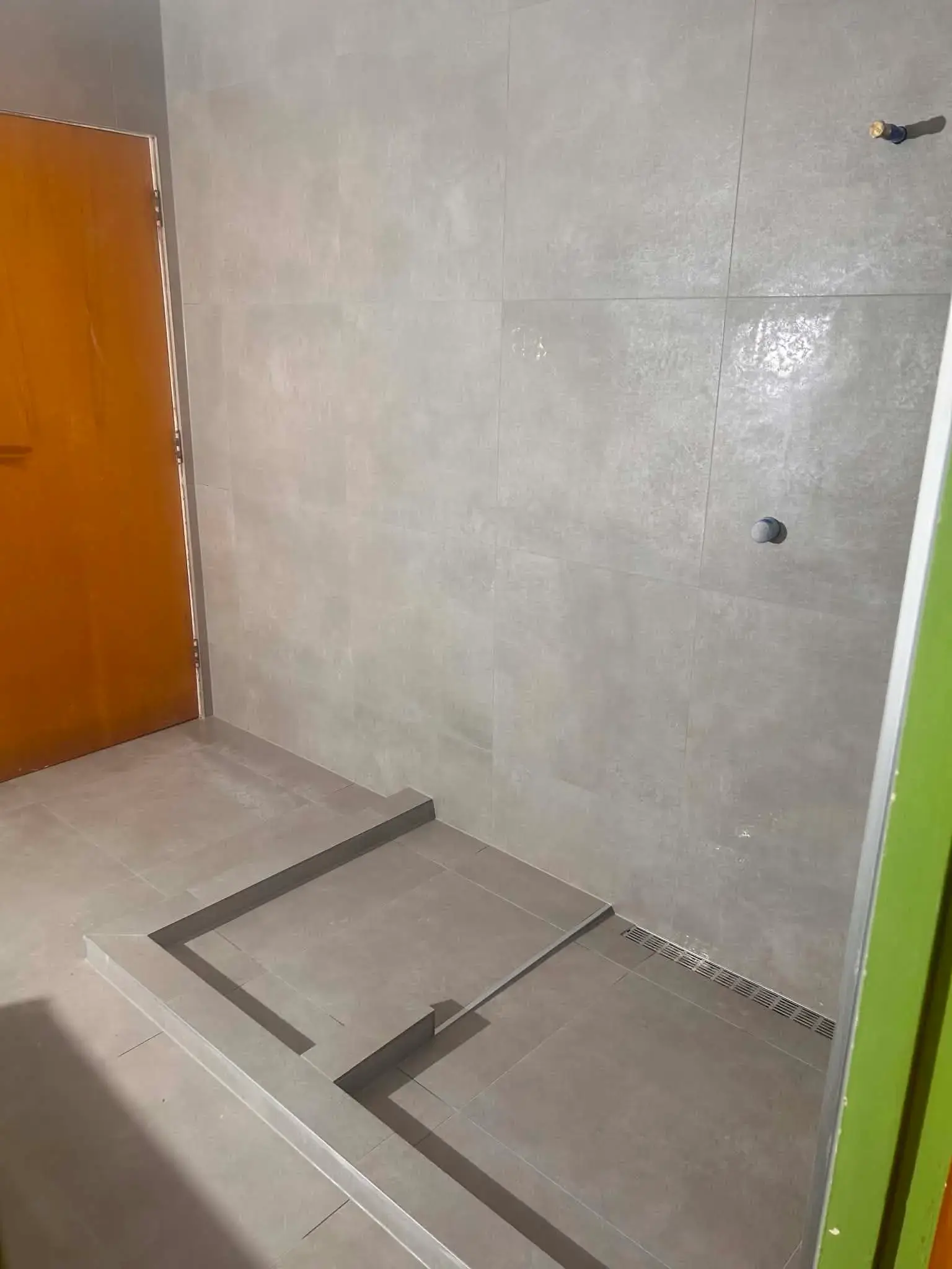 Walk-in shower with grey large-format tiles, tiled hob and linear drain set to fall