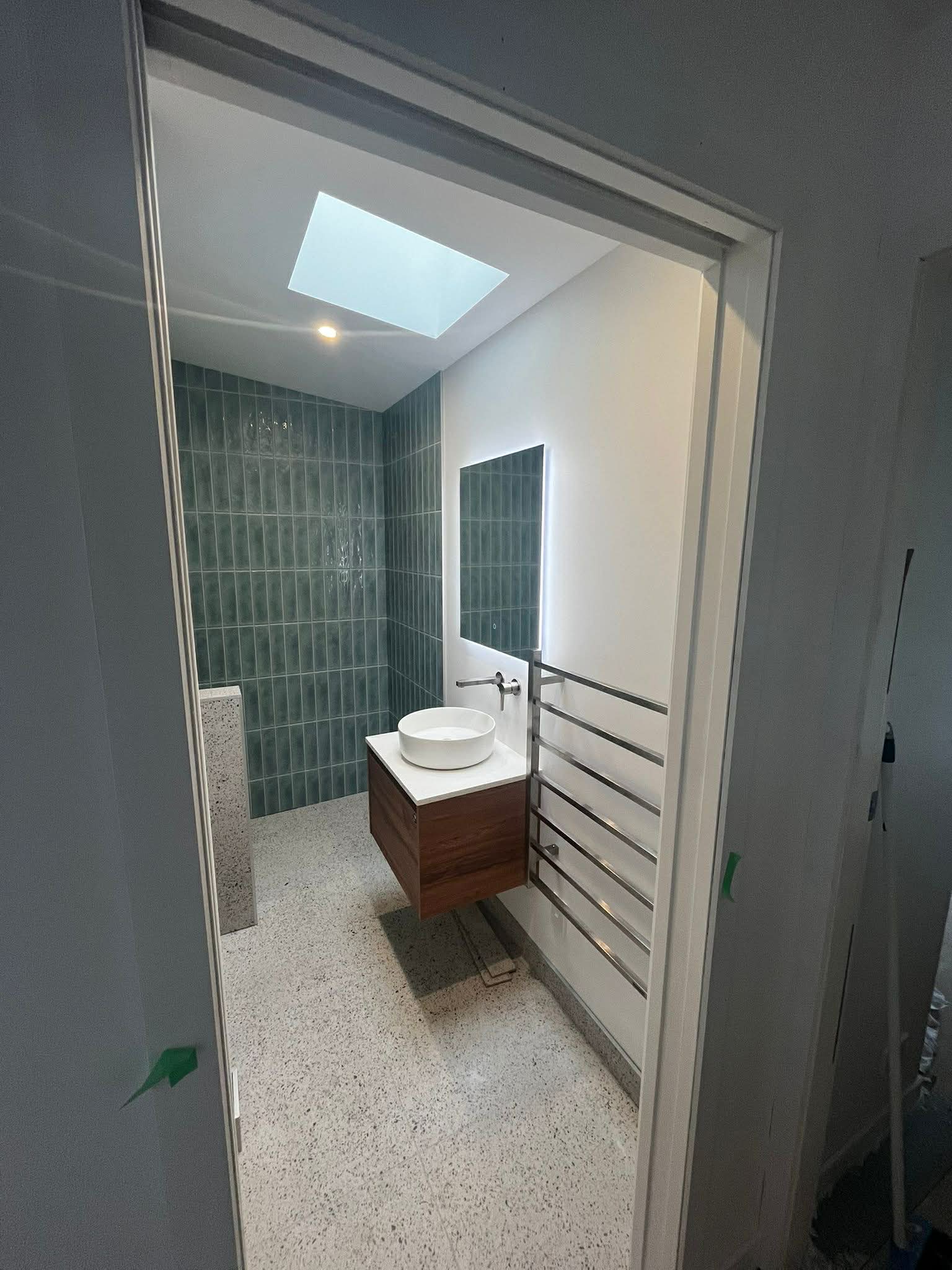 Modern designer bathroom with green subway tile feature wall, terrazzo floor, and skylight — Wellington bathroom renovation