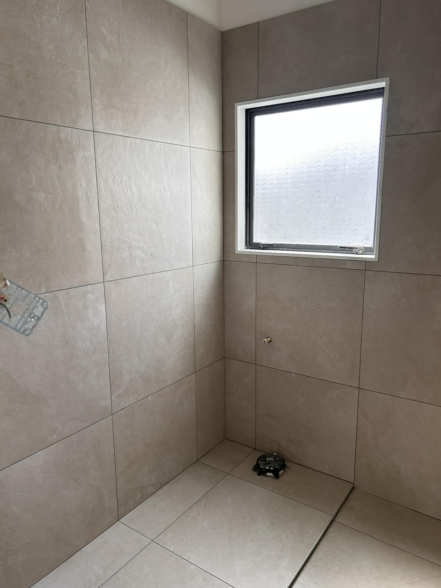 Walk-in shower with natural stone-look tiles and frosted privacy window — Wellington home